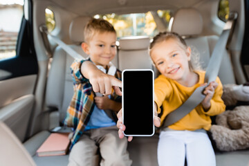 Smartphone with blank screen in hand of smiling kids on blurred background in car