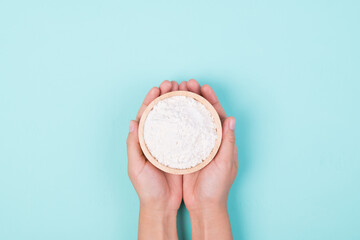 Wheat flour in a wooden bowl holding by woman hand on color background, Top view