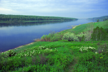 Fototapeta na wymiar Summer wide-angle panorama of the river, the picturesque shore and the cloudy sky. Wide calm river distance with gentle green banks. Typical landscape of central Russia. Siberia.