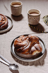 Cinnamon swirl brioche or Cinnamon roll bun and cups of cocoa on greige linen tablecloth. Homemade baked swedish cinnamon roll. Kanelbullar. Cozy winter breakfast