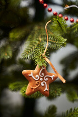 Christmas tree toy in the form of a star made of gingerbread with white patterns hangs on a green Christmas tree. red beads are visible in the background