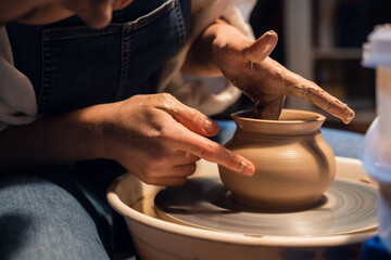 close-up of the hands of a potter when sculpting a vase from clay on a potter's wheel in the...