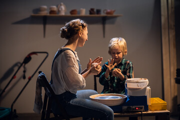 a pretty girl and a blond boy sculpt a plate on a potter's wheel in an art Studio