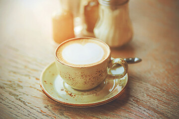 On a wooden table on a ceramic saucer is an elegant Cup of hot soft cappuccino, illuminated by sunlight. Refreshing coffee in the early morning.