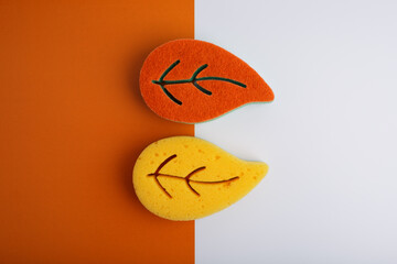 Flat lay with colorful leaf shaped sponges for home and dishes cleaning on orange and white background
