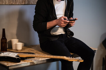 in a music Studio a guy sits on a table and plays a video game on his phone after a rehearsal