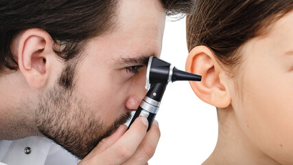 Otolaryngologist checking child's ear using otoscope. Hearing exam for girl close-up. Otitis media, ear inflammation