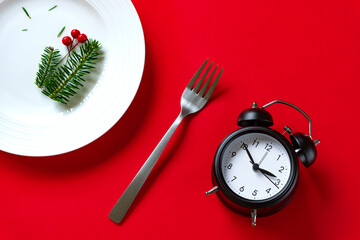 Fir branches, a plate and a clock on the table. Christmas business hours, winter meal times,...