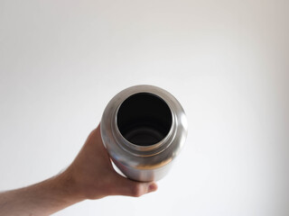 Eco-friendly steel water bottle in a male hand before a white backdrop