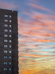 Tall brown brick skyscraper residential building with many windows against sunset sky.