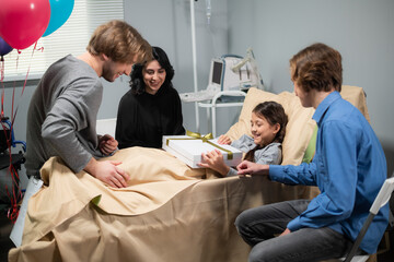 A little girl receives a present from her family, she is sick, staying in bed in a hospital. The...