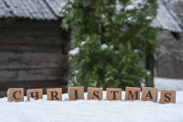 A word Christmas arranged from a wooden blocks with letters, on a snowed table.