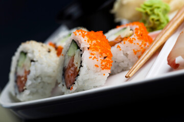 Sushi served on a white plate with chopsticks. Studio photo isolated on black background. Selective focus on object. Bright light setting.