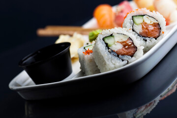 Sushi served on a white plate with chopsticks. Studio photo isolated on black background. Selective focus on object. Bright light setting.