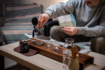 A man learns to conduct a tea ceremony at home on his own. Pours black ripe tea with clip into a teapot on a bamboo gongfu tray