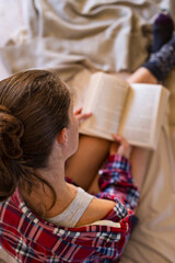 Woman in pyjamas reading book on bed