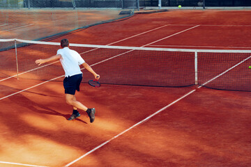 Fototapeta premium Back view of a man playing tennis on tennis court