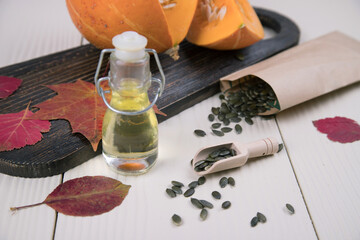 On a light background, a measuring wooden spoon with scattered pumpkin seeds, a bottle of pumpkin oil, and a cut pumpkin on a dark wooden Board. Alternative to traditional oil.