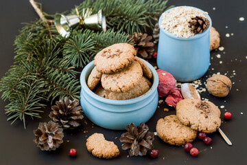Preparing for Christmas. A cup with homemade oatmeal cookies, a fresh cranberries, a spruce branch and pine cones on a dark background. Selective focus.