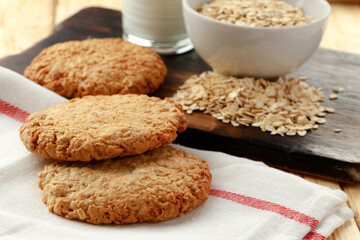 Oat cookies with oat flakes and cup of milk on wooden table