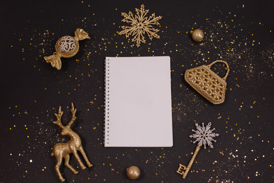Holiday golden decorations and white notebook on black background.