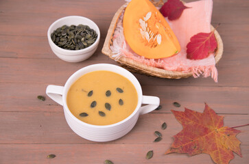 On a wooden background, a plate with pumpkin puree Soup, a piece of pumpkin, pumpkin seeds and autumn leaves. Horizontal orientation
