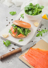 Fresh sandwich with bagel and salmon, cream cheese and wild rocket on white board with smoked salmon pack and knife
