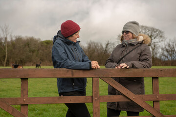 Two female friends talking outdoors leaning on a wooden fence