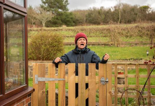 Senior woman shouting over a wooden gate outdoors in winter 