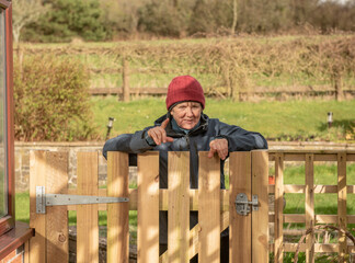 Senior woman pointing and laughing leaning over a wooden gate outdoors 