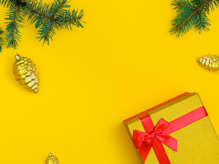 christmas background: red gift box with shiny lid, fir branches and gold cones on yellow background