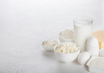Fresh dairy products on white table background. Glass of milk, bowl of baking flour, cottage cheese...