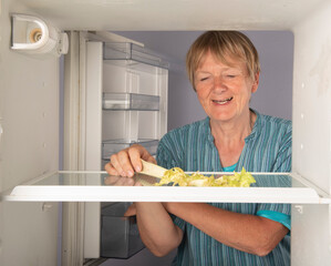 Senior woman reaching inside an empty fridge for celery looking happy 