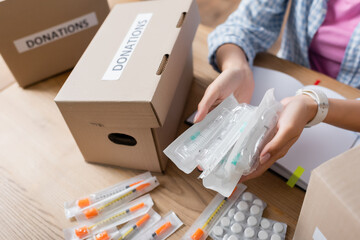 Cropped view of volunteer holding syringes near pills and packages with donations lettering