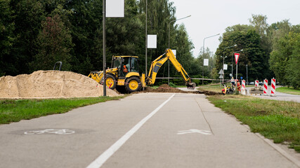 Road construction works. Asphalt road. Pedestrian and bicycle path. Yellow excavator digs ground.