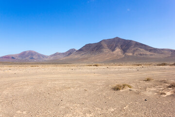 Fototapeta na wymiar Empty desert volcanic landscape on sunny day in Lanzarote with mountains on background. No vegetationon on arid land in Canary Islands. Travel adventure concept