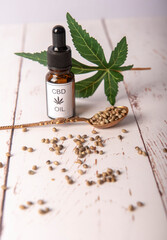 Vertical image of CBD oil with cannabis seeds on a white wooden background 