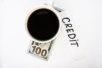 A Cup of coffee is on a hundred-dollar bill next to a piece of paper with the word credit written on it. Concept photo
