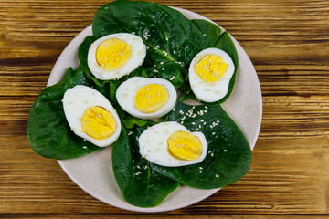 Boiled eggs with fresh spinach leaves and sesame seeds on wooden table. Top view