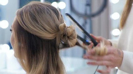 Young brunette woman hairdresser makes styling on the long hair of the blonde girl.
