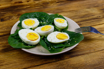 Boiled eggs with fresh spinach leaves and sesame seeds on wooden table