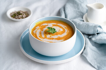 Pumpkin soup with coconut milk in blue bowl, vegetarian dish, healthy dieting food on white tablecloth, side view