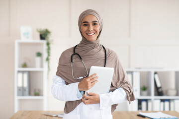 Happy female doctor in hijab posing with digital tablet - obrazy, fototapety, plakaty