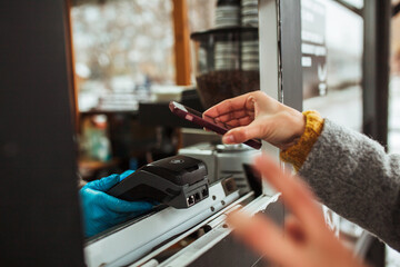 Closeup of a payment terminal and a mobile phone in woman's hands paying for coffee. Contactless payment at a cafe. Street food and drinks, coronavirus spread prevention concept.