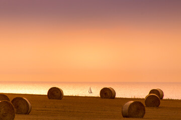 coucher de soleil sur la Manche avec un voilier devant des prés avec des bottes de foin