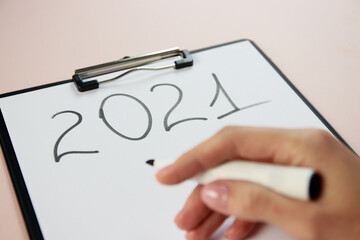 girl's hand close up with a marker written on a sheet of A4 paper with numbers 2021 New Year makes a plan