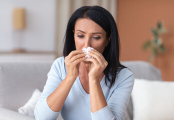 Sick mature woman sneezing and crying, holding tissue paper