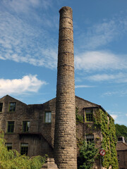Fototapeta na wymiar old mill building and tall chimney with blue cloudy sky in hebden bridge west yorkshire