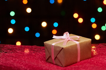 Christmas or New Year gift box on red cloth against a background of colorful lights. Close-up,...