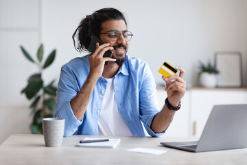 Easy Payments. Indian Freelancer Guy Holding Credit Card And Talking On Cellphone
